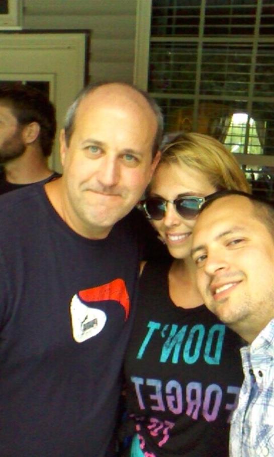 Three friends smile and pose together in a lively environment, enjoying each other's company.