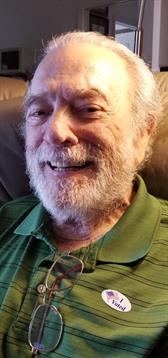 An elderly man with a beard smiles warmly while sitting comfortably in his chair.