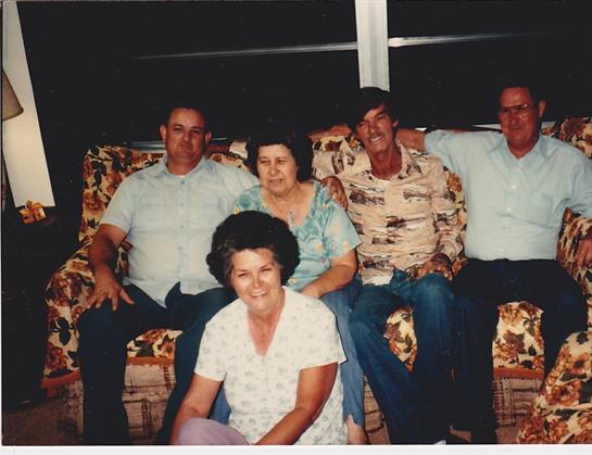 Five family members relax together on a couch, sharing joy and laughter in a cozy setting.