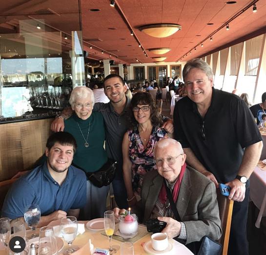 Six family members at a table, smiling, sharing drinks, and enjoying a meal together.