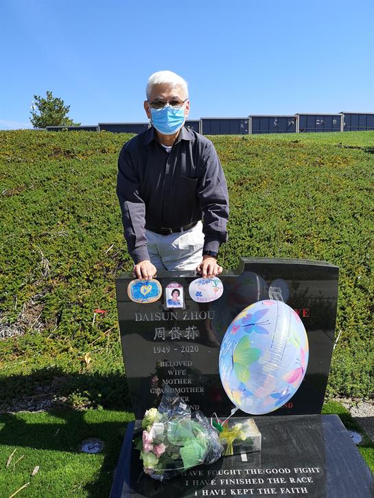 Individual stands by a grave, placing flowers and showing respect on a clear day.