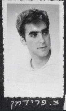 A young man wears a plain shirt and gazes thoughtfully towards the camera while being photographed.
