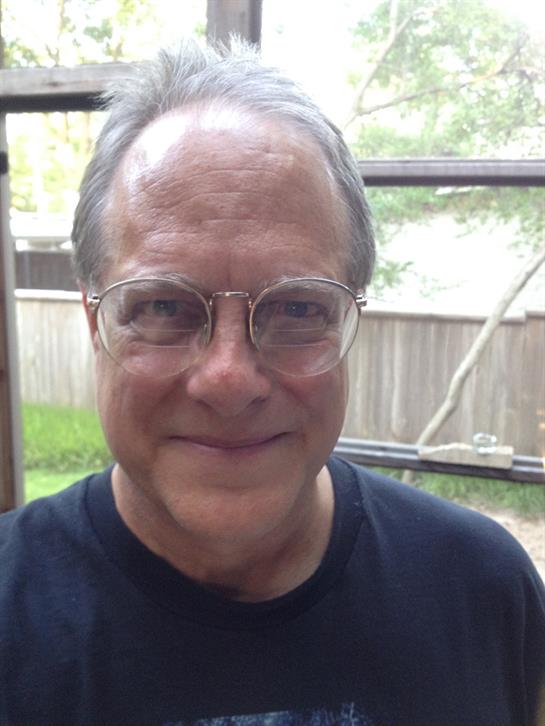 A cheerful man wearing glasses takes a selfie in his backyard on a bright spring day.