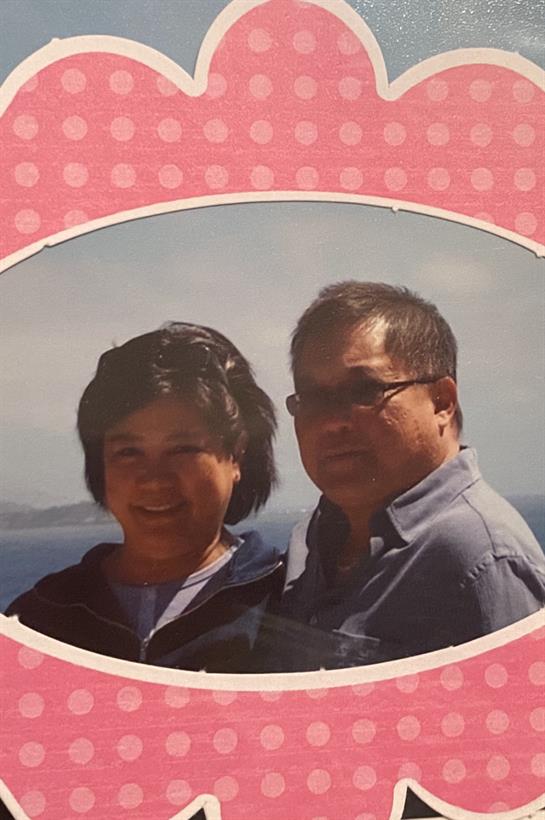 Two people stand together, smiling, and enjoying a pleasant day by the water's edge.