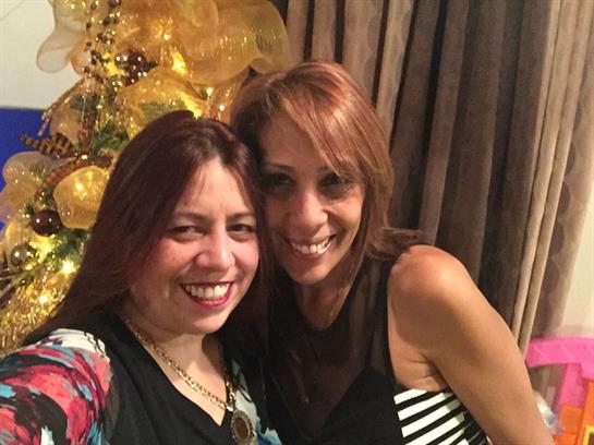 Two friends smile and embrace at a lively gathering adorned with bright decorations.