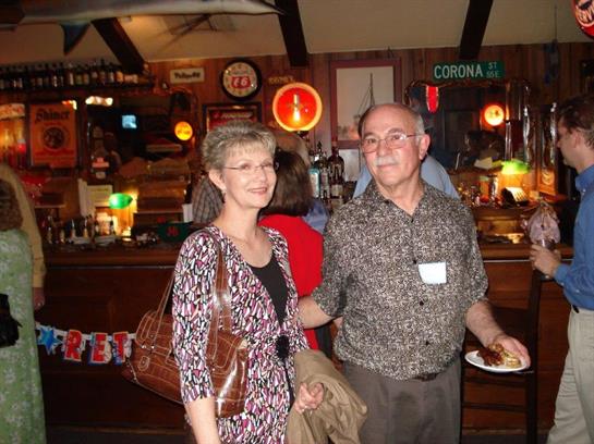 A man and woman smile while mingling at a festive event, surrounded by lively decorations.