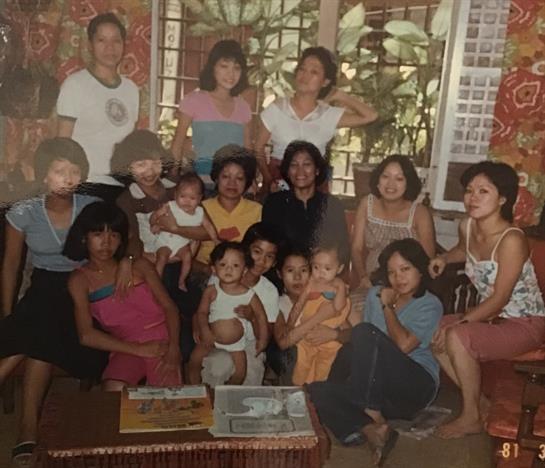 A large family gathering with women and children smiling and enjoying each other's company indoors.