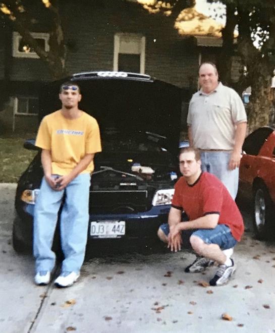 Two men crouch and one stands by a modified car, showcasing their shared interest in vehicles.
