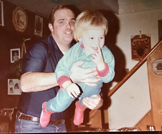 A father lifts his child in colorful pajamas in a cozy living room, sharing a joyful moment.