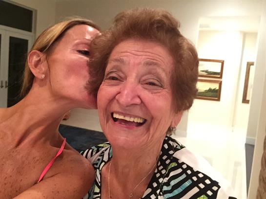 Joyful interaction between a woman and her grandmother sharing a loving kiss at home.