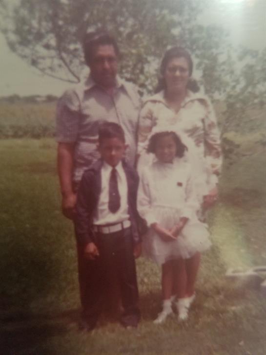 A joyful family stands together in a lush outdoor setting under bright daylight, smiling happily.