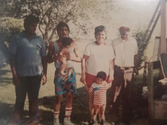 Group of family members stands together in a park under bright sunlight, sharing a happy moment.