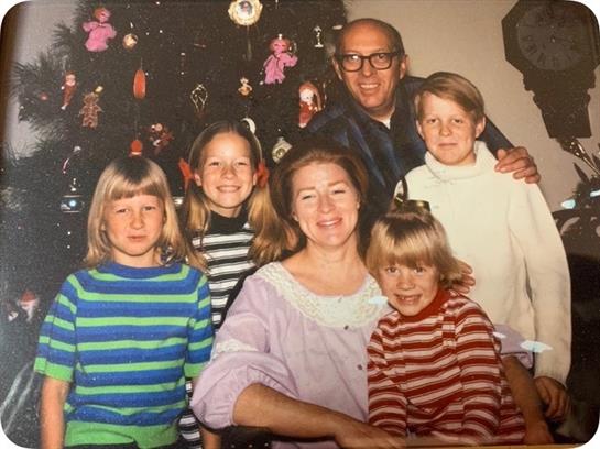 A group of children and adults smiles joyfully together in a lively, decorated room.