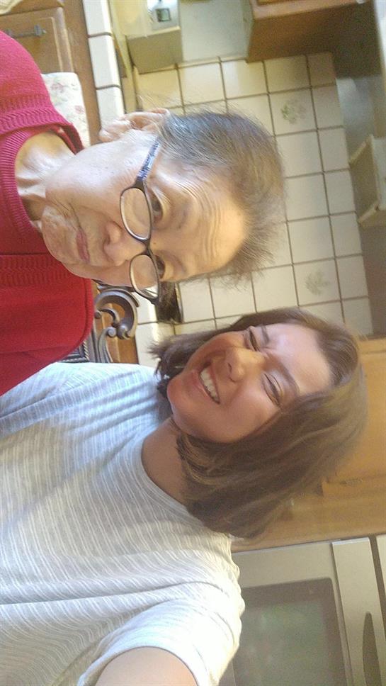 Two women pose together with playful expressions in a warm, inviting kitchen filled with sunlight.