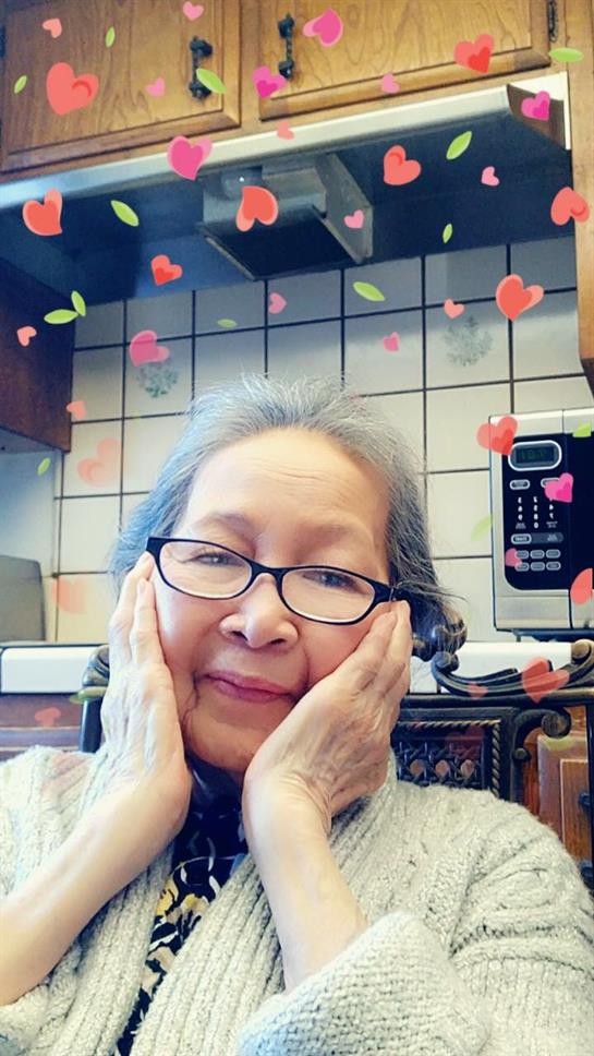 An elderly woman with glasses gently touches her face in a welcoming kitchen, radiating happiness.