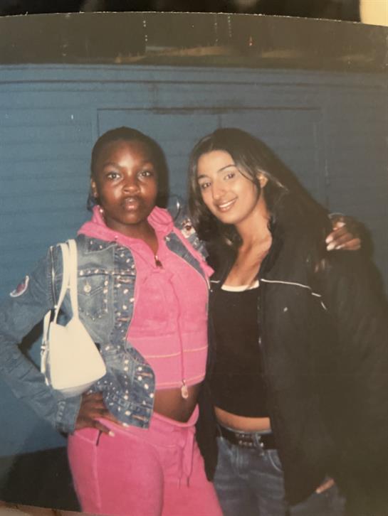 Two friends stand side by side, smiling and enjoying their time together at a vibrant social event.