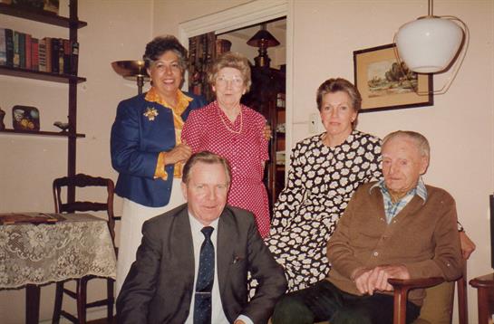 Five family members gather in a warm living room, each enjoying the company and memories shared.