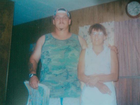 A couple stands close, smiling happily, in a dimly lit room with wooden walls.