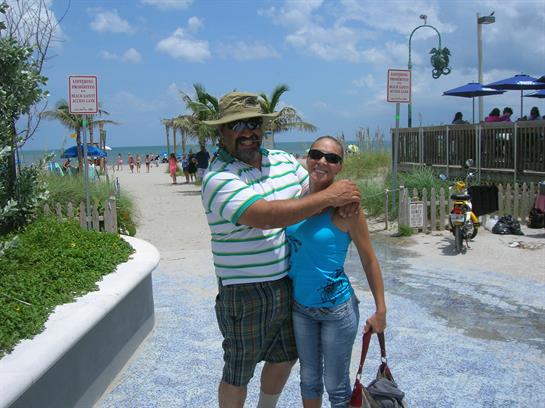 Two people smile while standing on a beach walkway, enjoying their time in the sun.