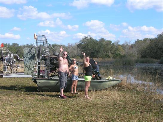 Friends enjoying sunshine and relaxing by an airboat on a clear day near a beautiful lake.