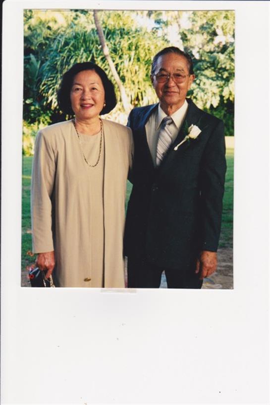 Happy couple stands closely together in a vibrant garden setting, dressed for a special occasion.