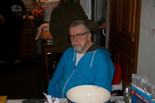 An older man with glasses looks contemplatively while seated at a kitchen table.