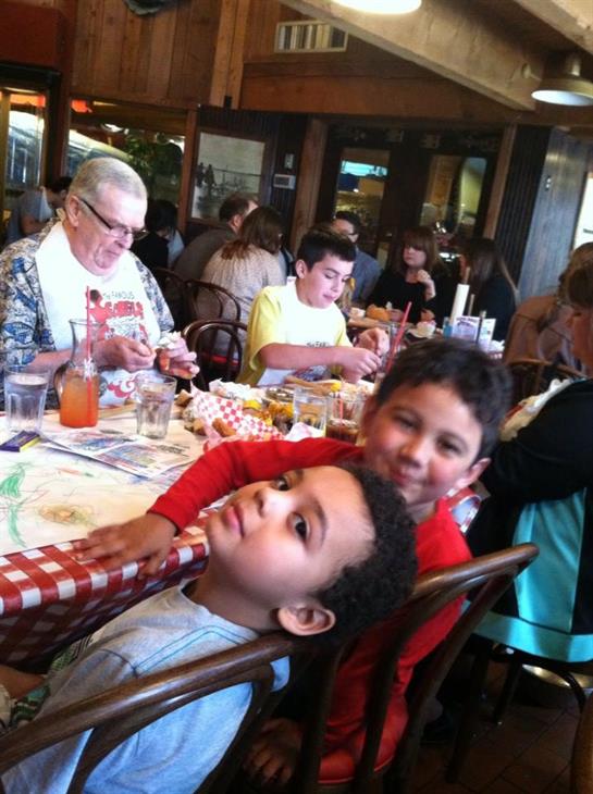 Children smile and pose while adults enjoy a relaxed meal at a bustling restaurant.