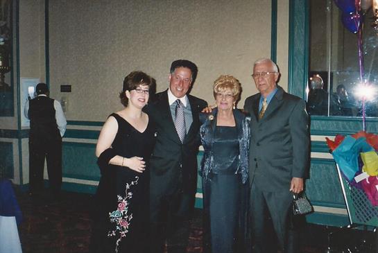 Four individuals dressed in formal attire gather for a group photo at a celebratory event.