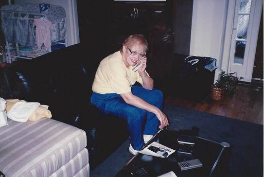 An older man sits on a couch, talking on the phone amid video equipment.