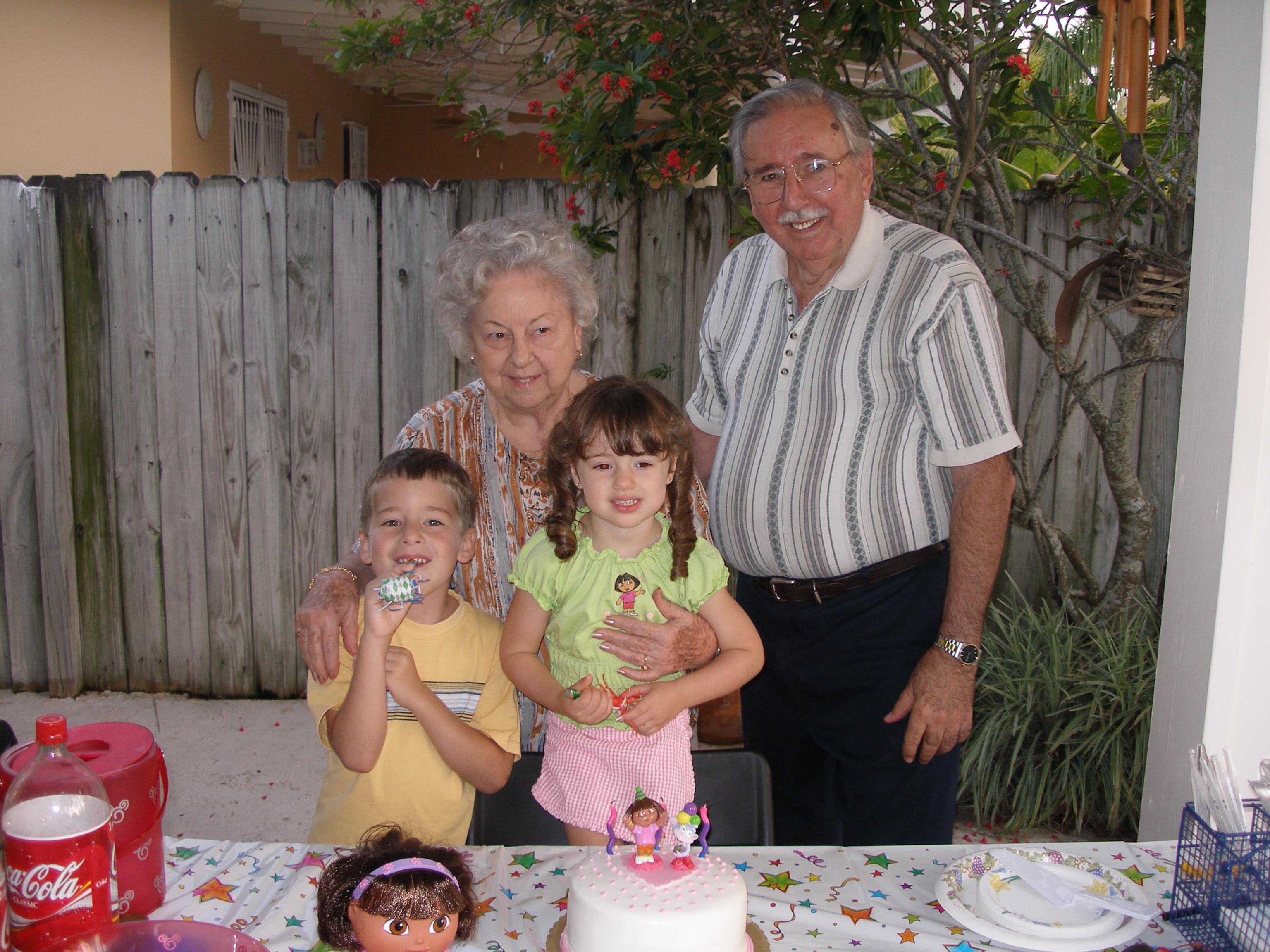 Grandparents pose with their grandchildren at a joyful birthday celebration outdoors.