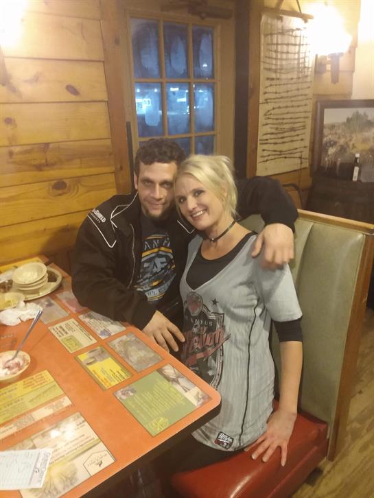 A couple sits closely together at a wooden table, smiling and enjoying their meal in a warm setting.
