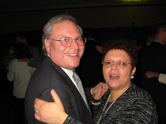 Two people dance happily together in elegant attire at a lively evening gathering.