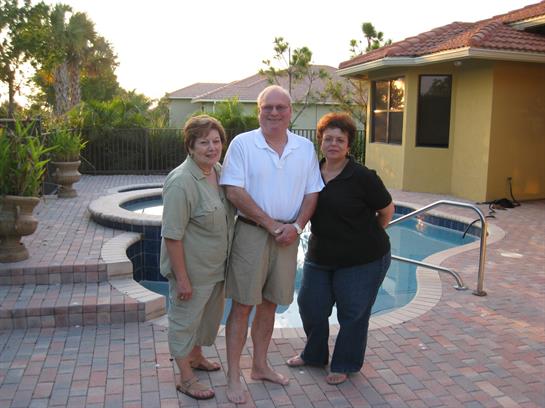 Three friends stand together smiling near a sparkling pool, enjoying a warm evening ambiance.