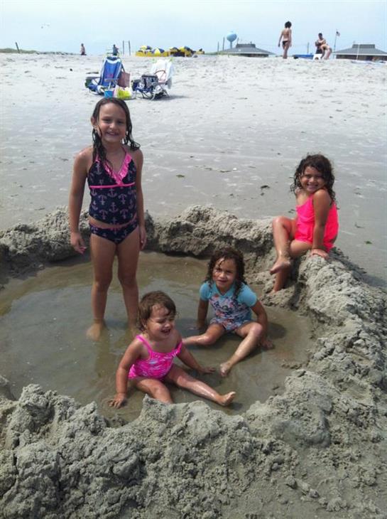 Four children happily play inside a sand pool at the beach, enjoying the warm weather and waves.