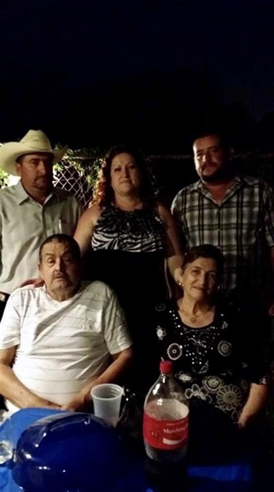 Five family members stand and sit together outdoors, enjoying each other's company at night.