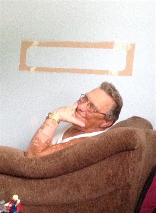 An older man sits comfortably on a couch, thoughtfully resting his chin on his hand.