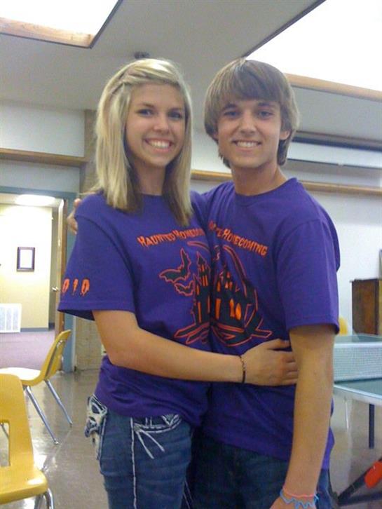 Two teens happily smile and hug in matching shirts at a community event.