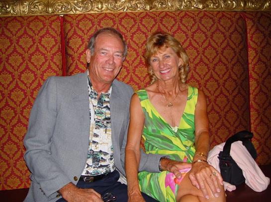 Two people sit comfortably together, smiling warmly at each other in an elegant location.