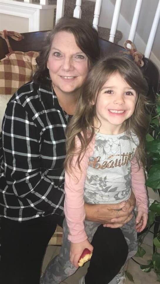 A woman with long dark hair and a young girl smile warmly in a cozy indoor setting.