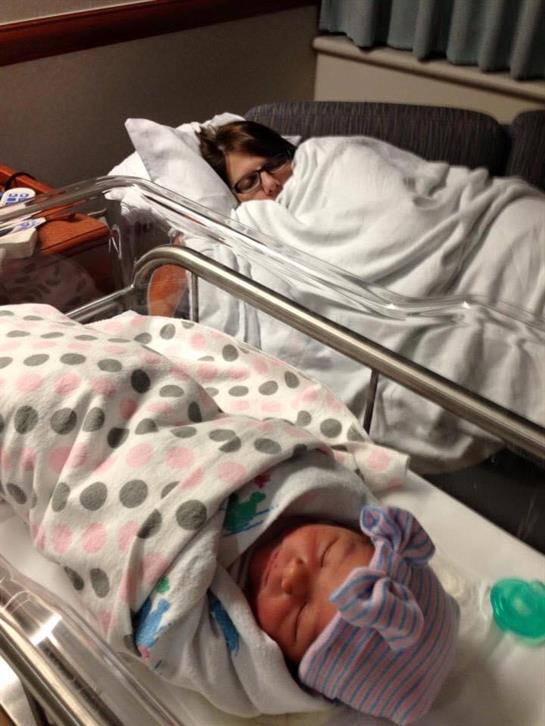 A mother relaxes in a hospital room while her newborn sleeps peacefully nearby.