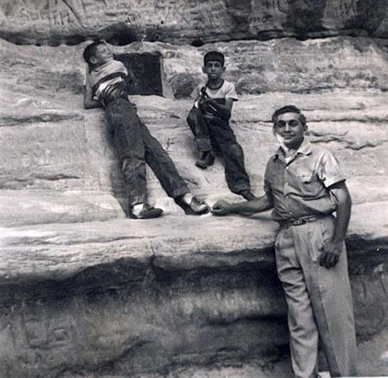 Two boys climb rocks as an adult supervises their exploration in daylight.
