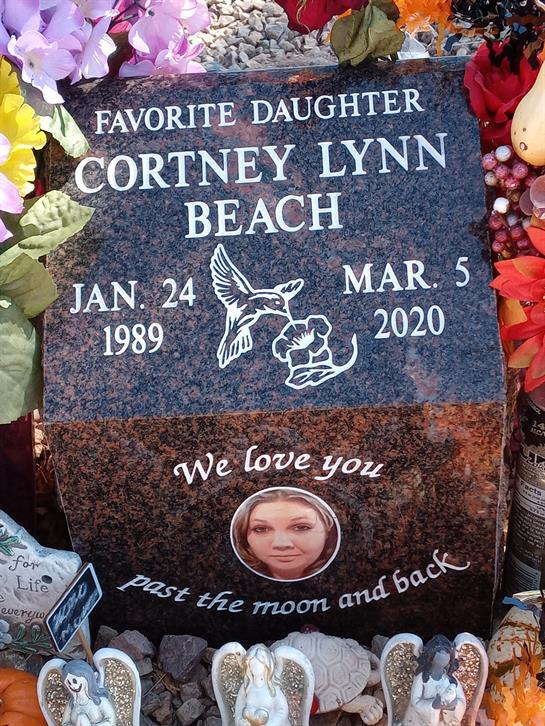 A decorated memorial stone for Cortney Lynn Beach, adorned with flowers and tributes.