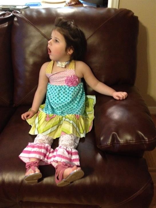 Young girl with a surprised expression sits on a leather chair in a cozy indoor setting.