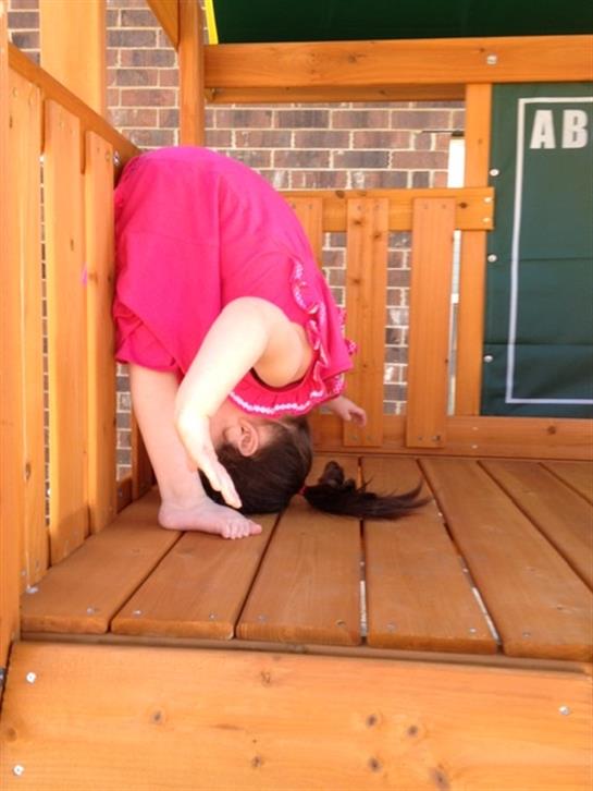 A girl in a pink dress does a headstand on a wooden deck, showing her balance.