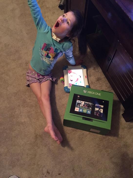 A young child sits on a carpet, joyfully interacting with a gaming console and surrounded by toys.