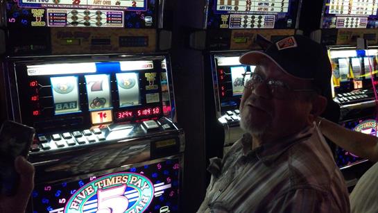 Man smiles while playing a slot machine in a casino, surrounded by bright lights and sounds.