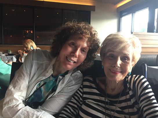 Two friends smile while seated at a table in a welcoming restaurant.