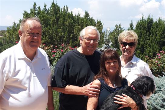 Friends stand together in a lush garden, enjoying each other's company under a bright sky.