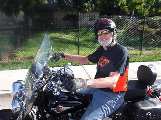 Elderly man smiles while riding his motorcycle on a warm sunny day in a quiet area.