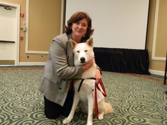 A woman kneels beside a service dog, highlighting their bond in a conference setting.